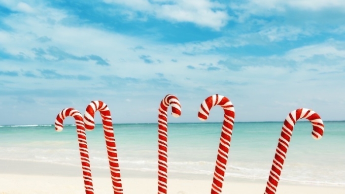 Christmas candy canes taking a tropical beach vacation for a winter holiday. They stand as a group of friends, traveling together and having fun in the white sand along the aqua blue water of the Caribbean Sea, Mayan Riviera, Mexico.